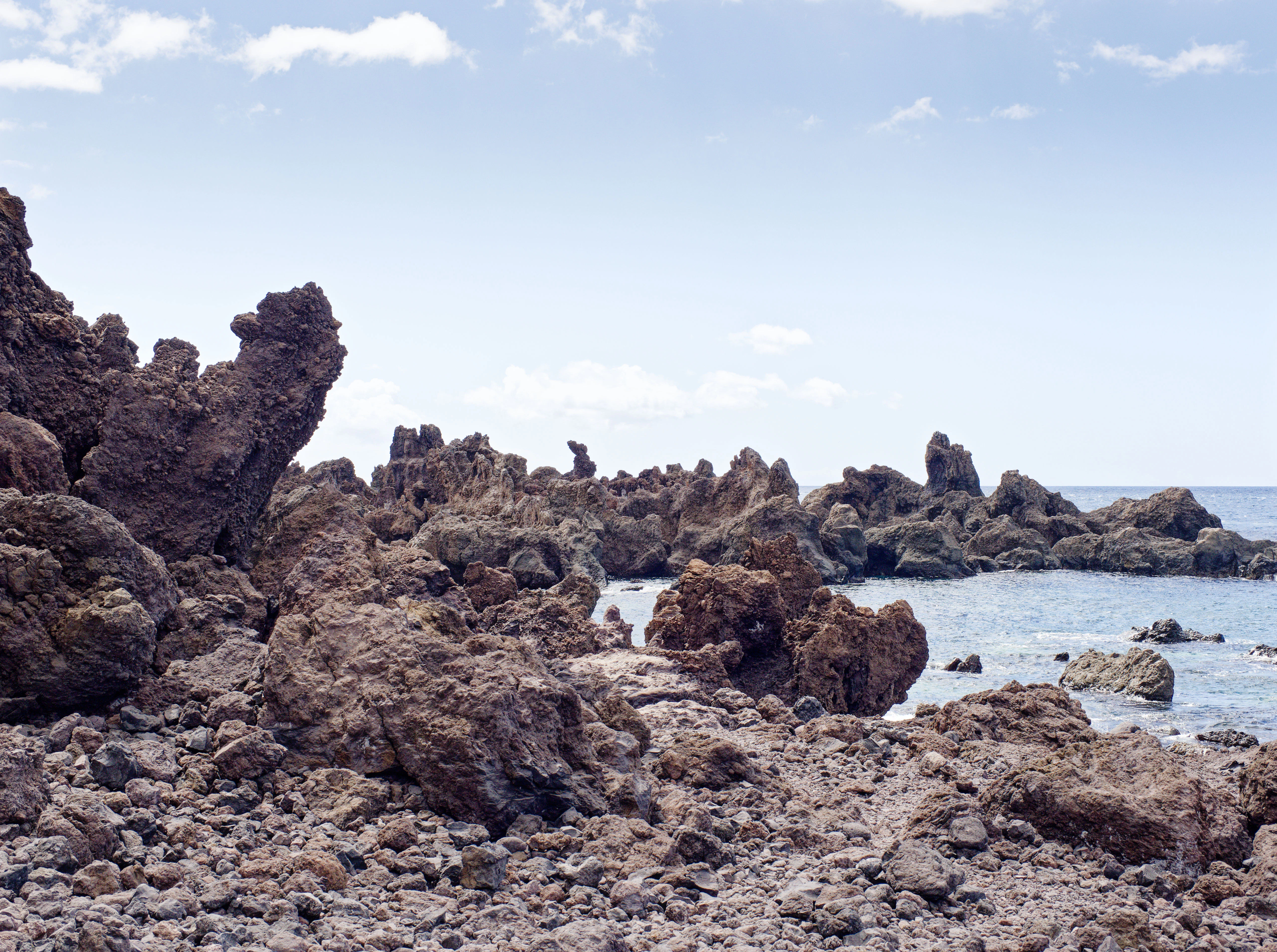 Jagged volcanic rocks line a rocky coastline with calm ocean.