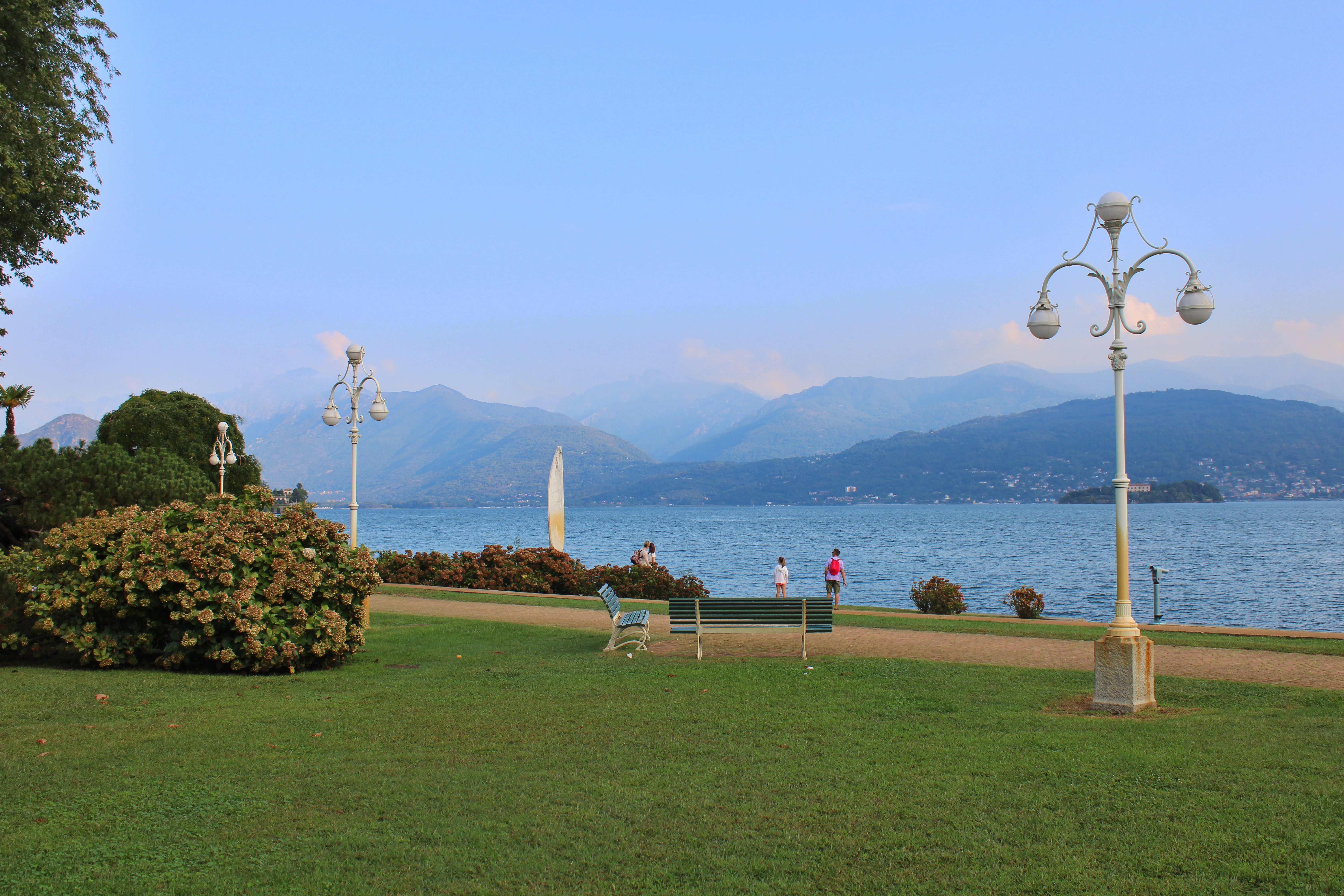 Lush green park beside a calm lake with mountains beyond.