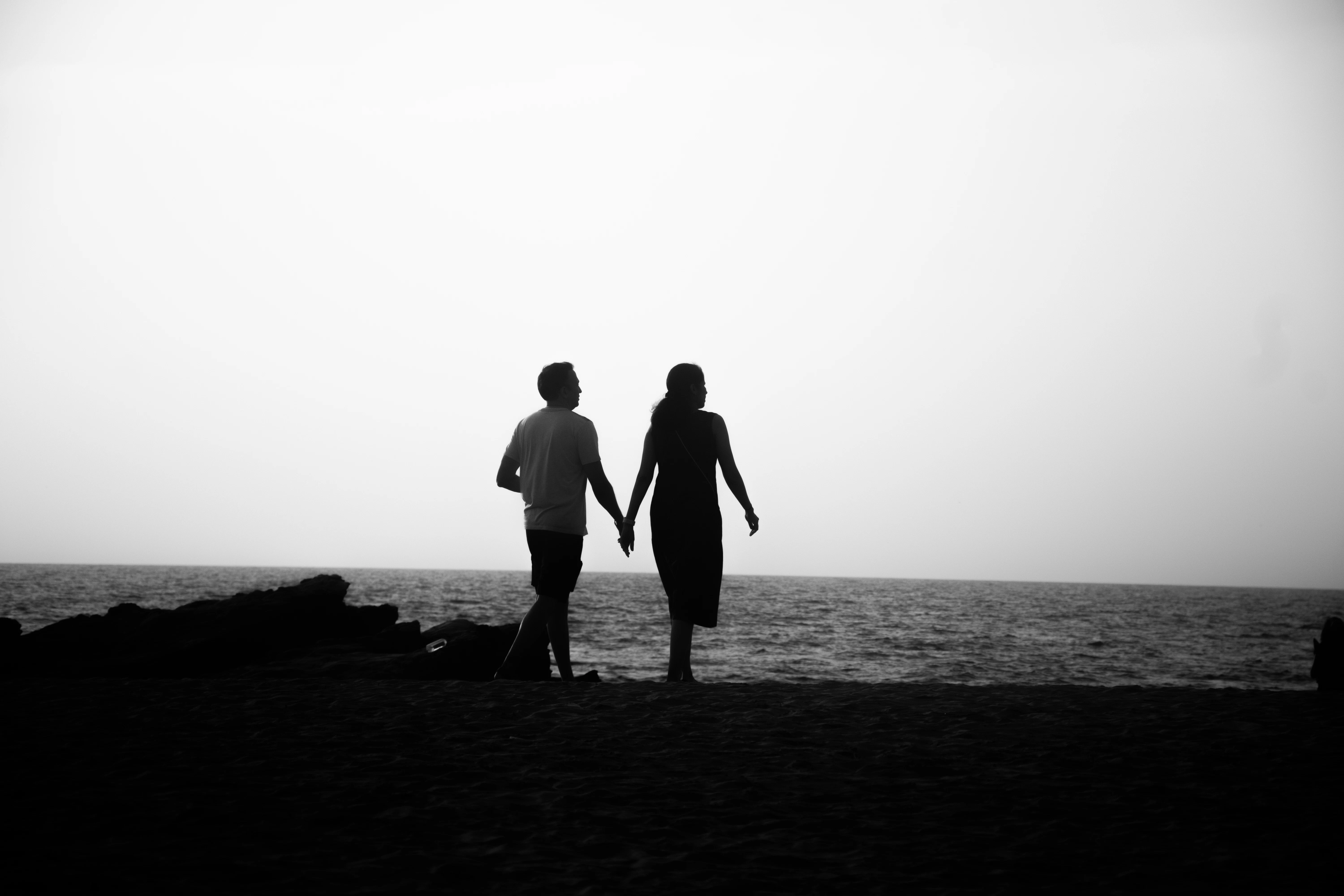 Couple walks hand-in-hand along the shore.
