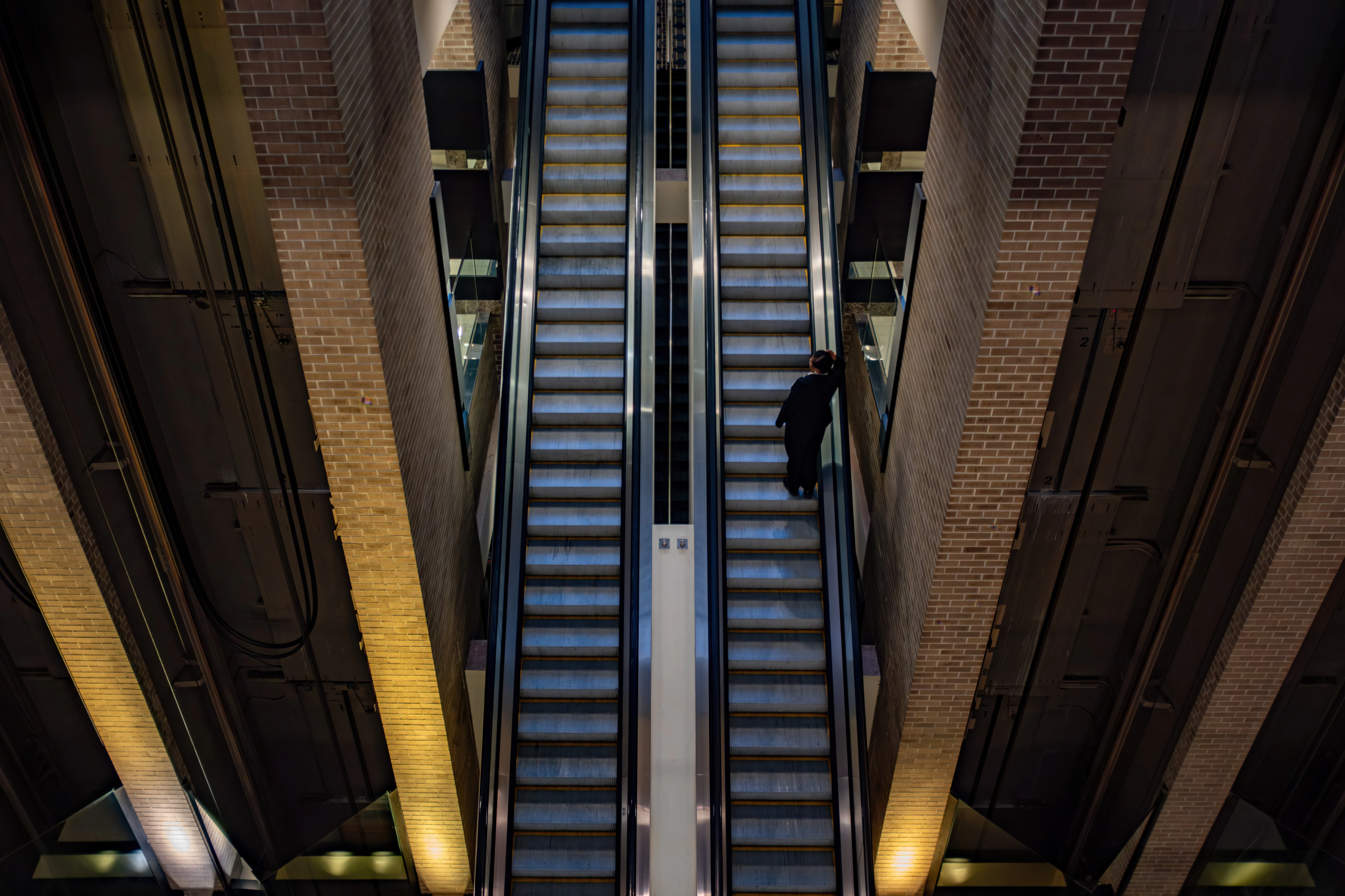 A person rides an escalator between illuminated brick walls.