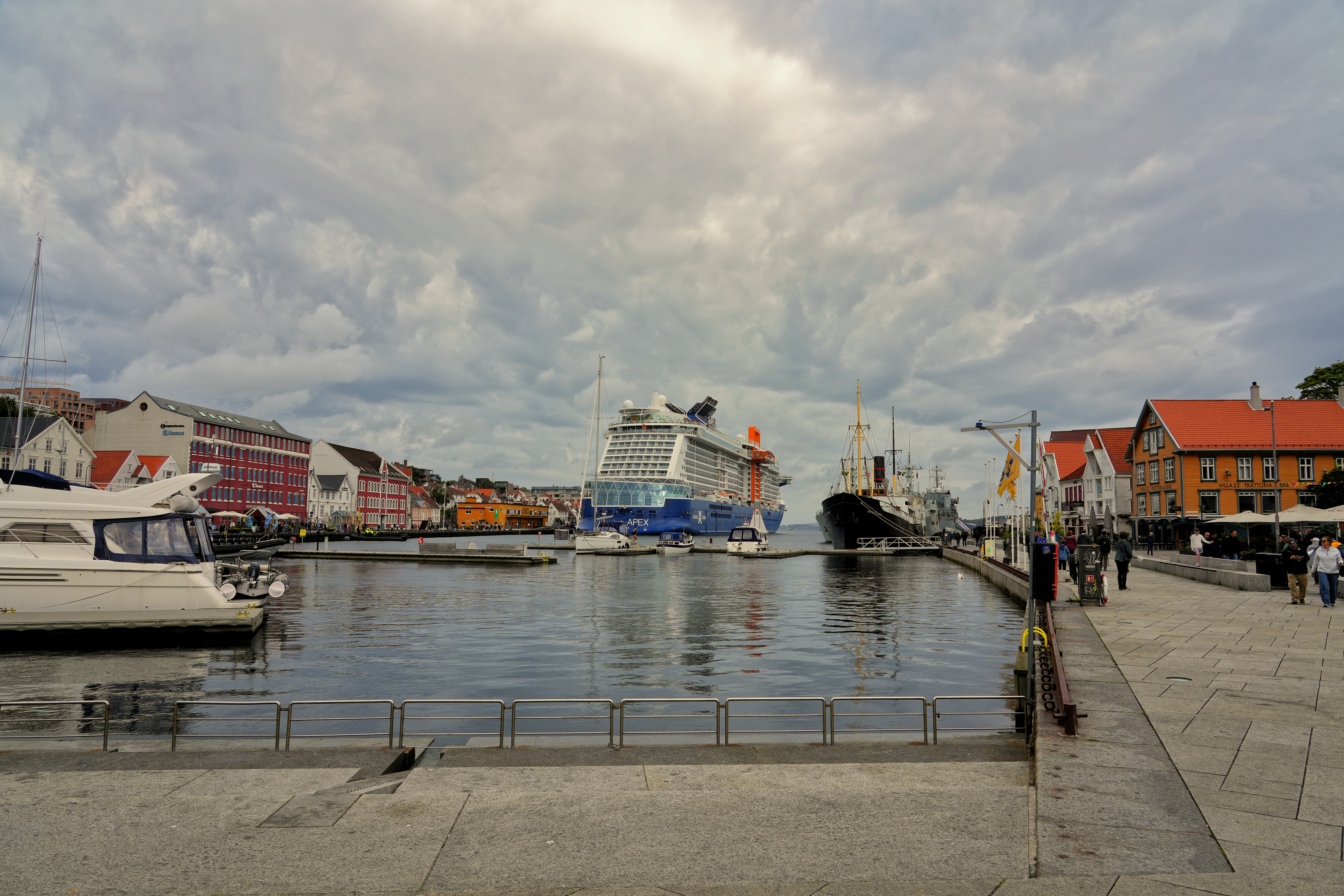 Boats docked in a harbor with buildings and cloudy sky.