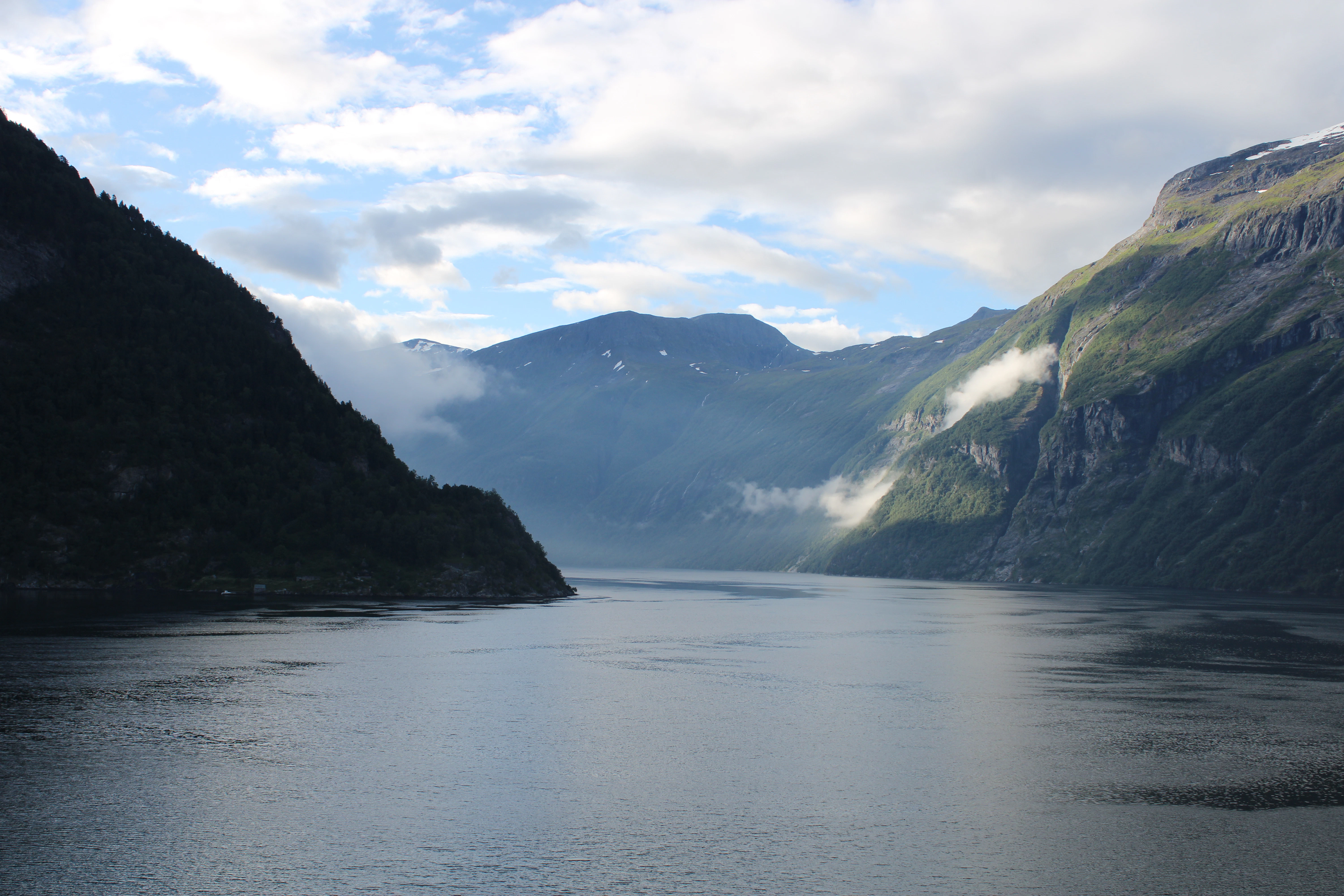 Calm water flows between majestic, cloud-kissed mountains.