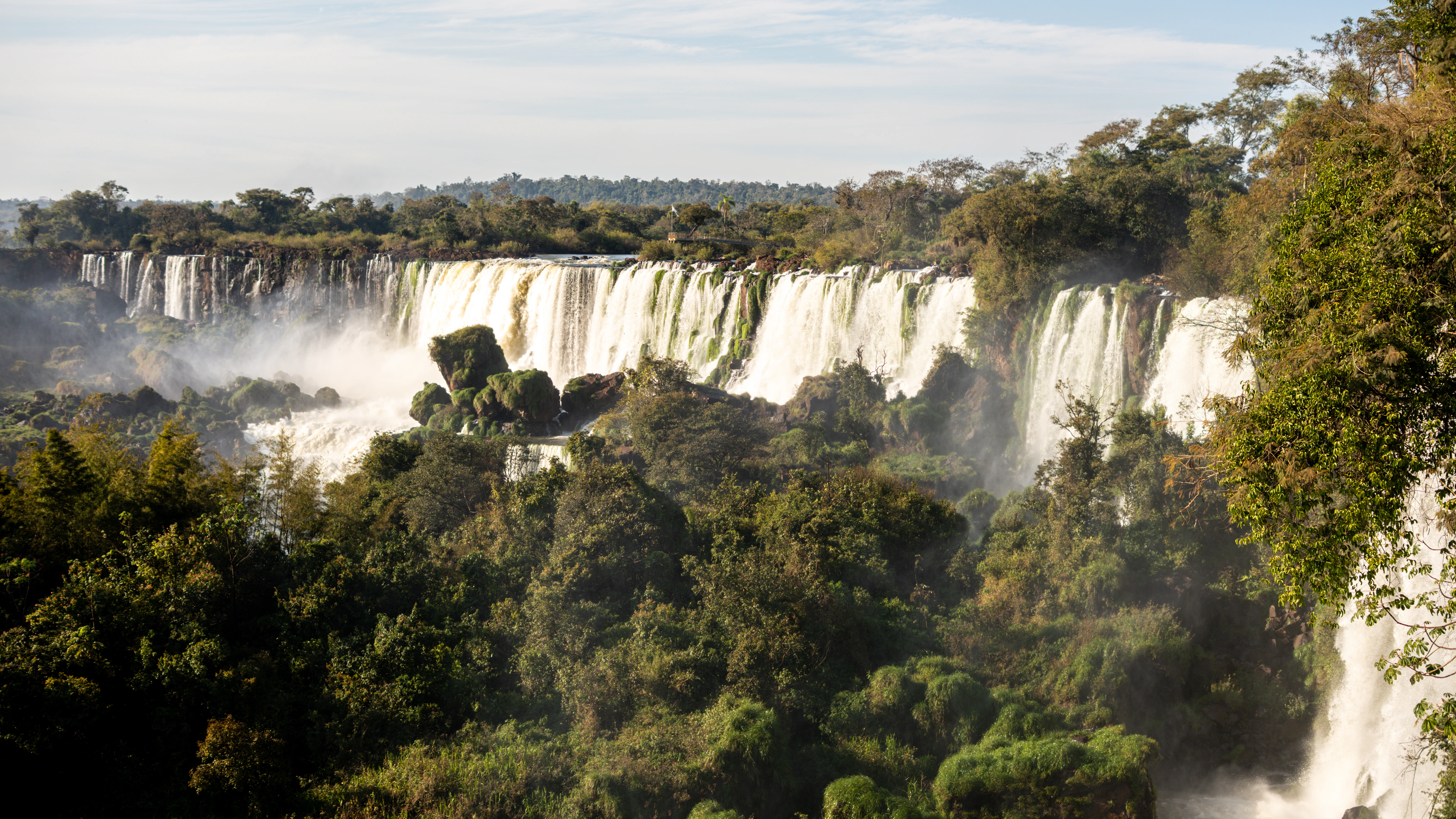 A wide waterfall cascades through lush green jungle foliage.