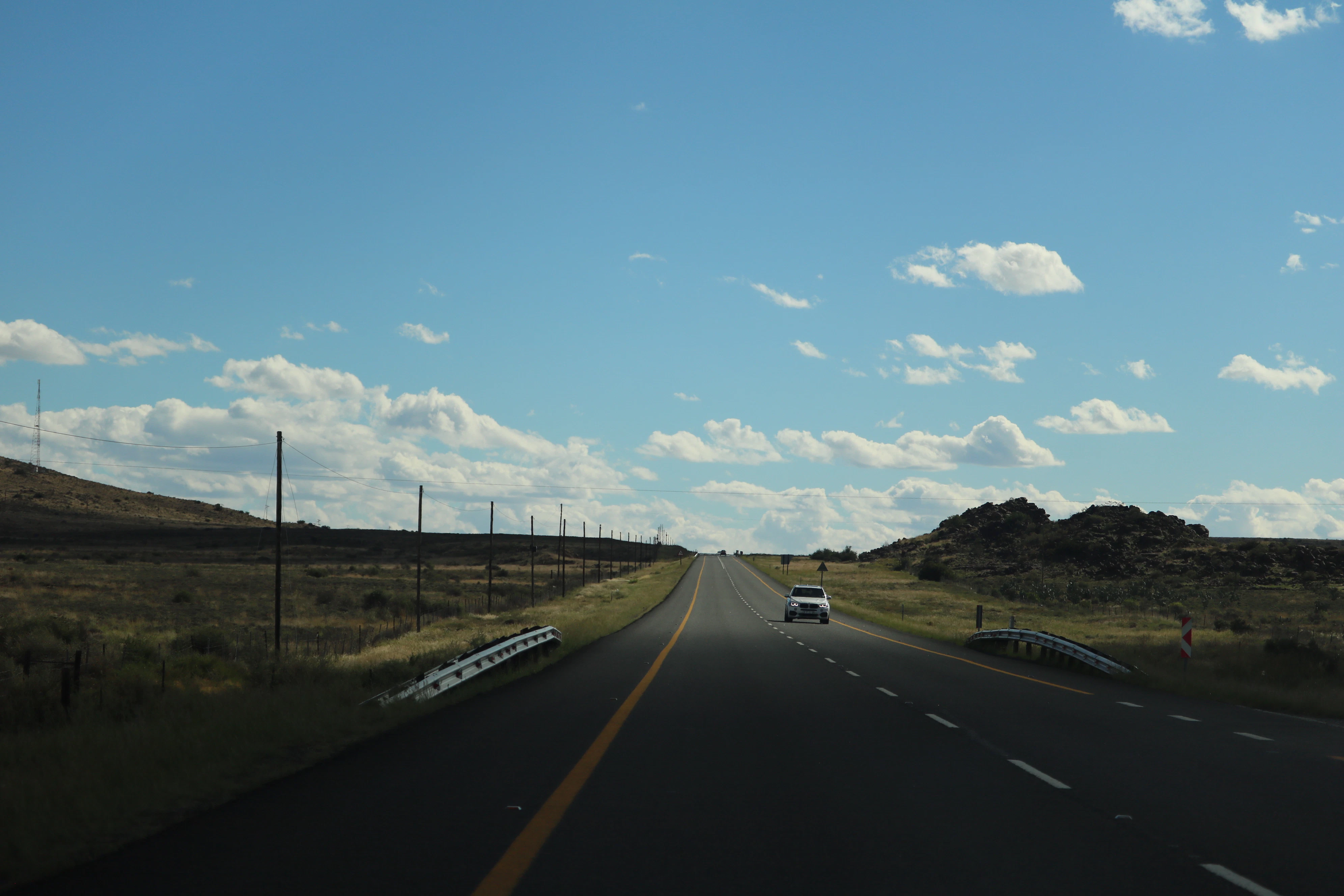A car drives down a highway under a cloudy sky.