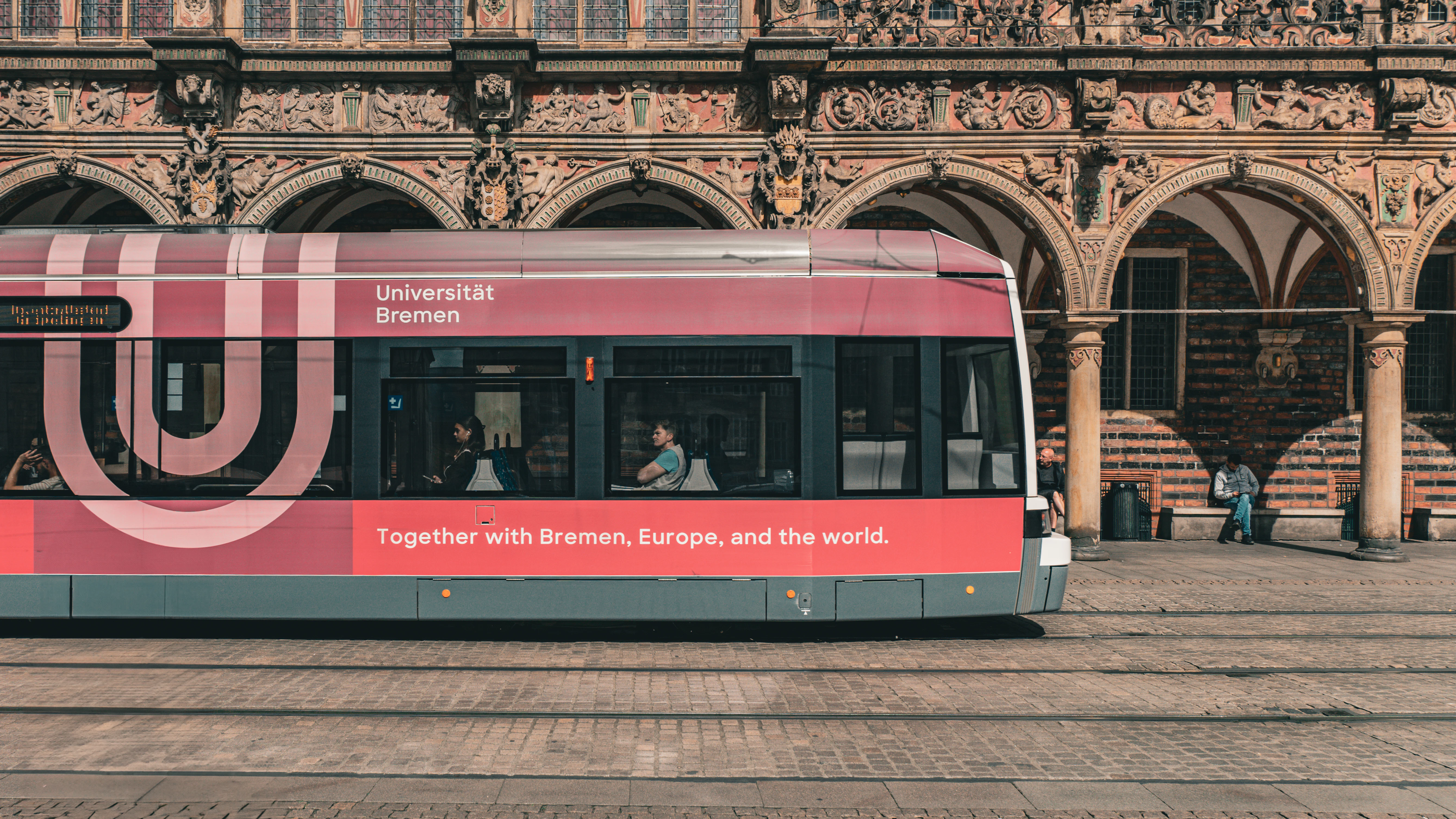 Red tram with advertisements passes ornate building