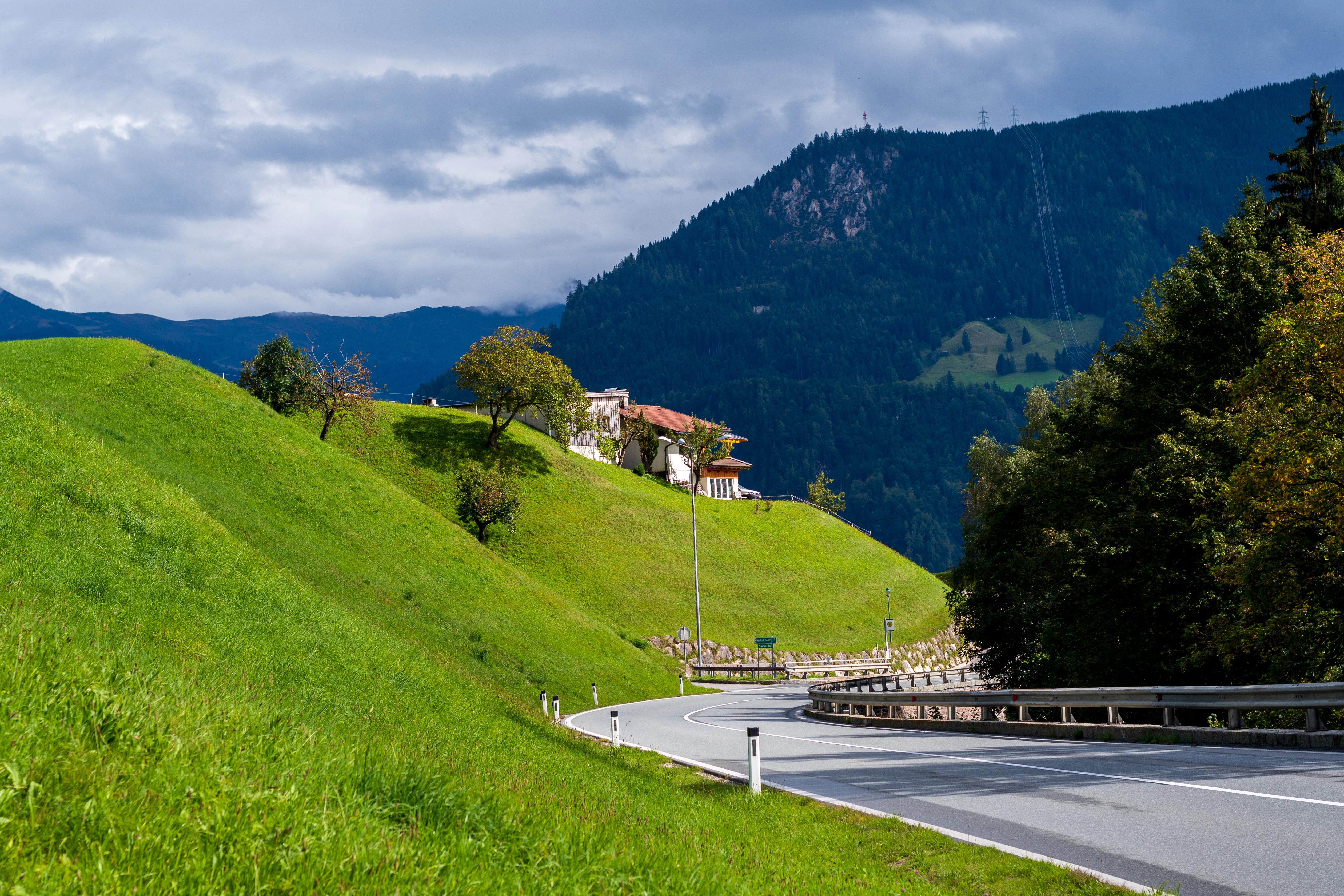a road leading to a house on a hill with trees and mountains in the background