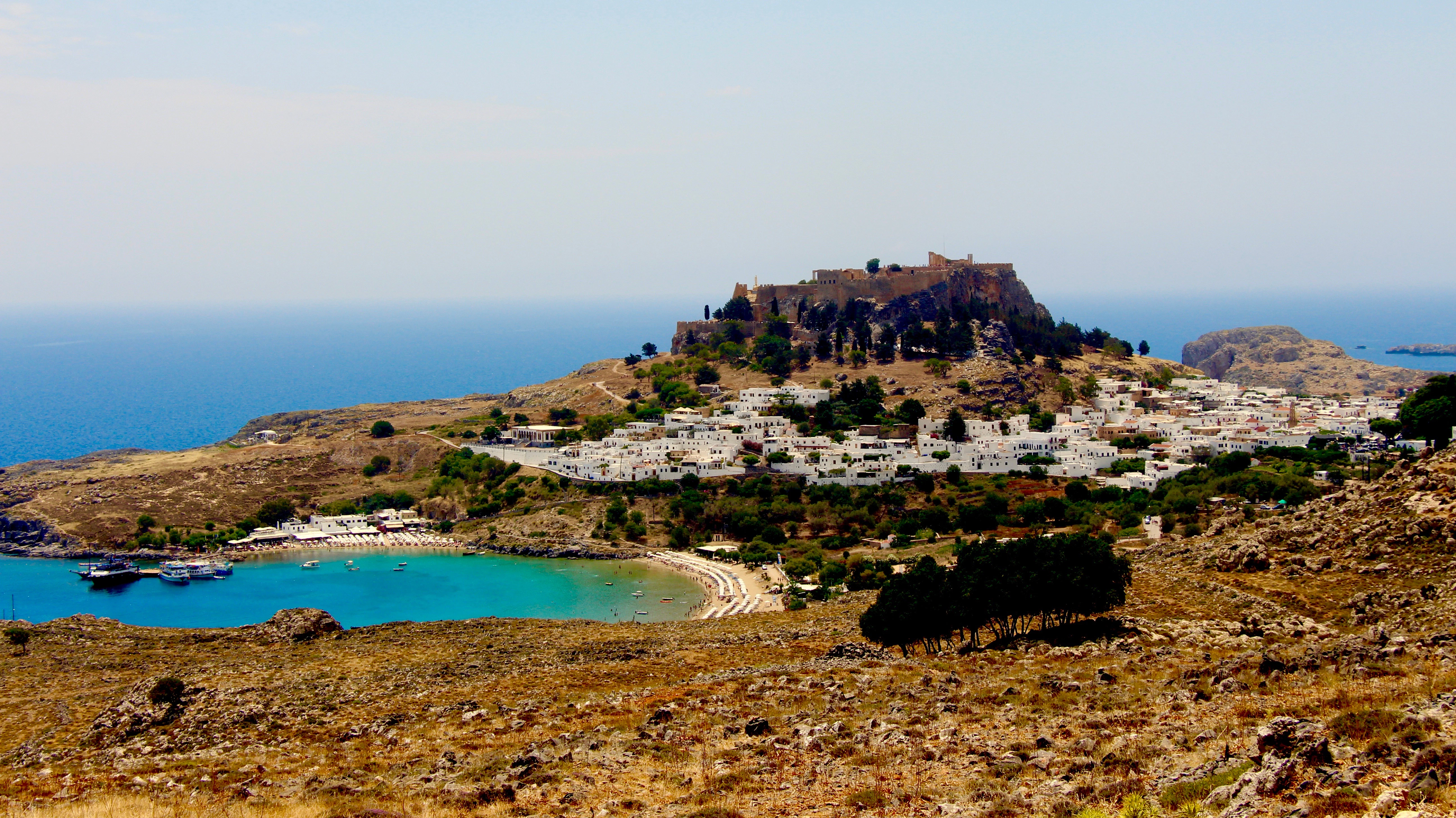 brown and green mountain beside blue sea under blue sky during daytime