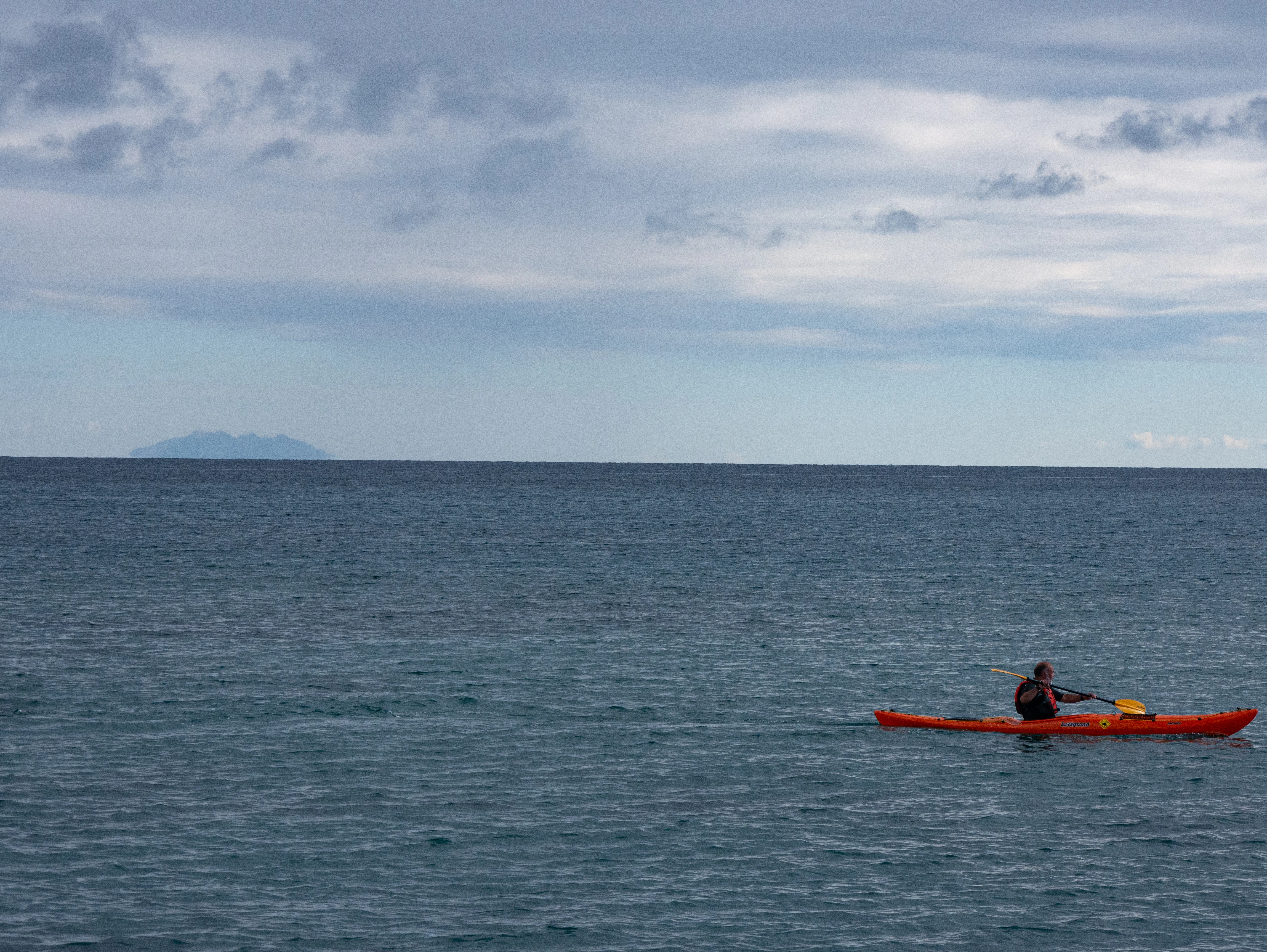 A person in a red kayak in the middle of the ocean