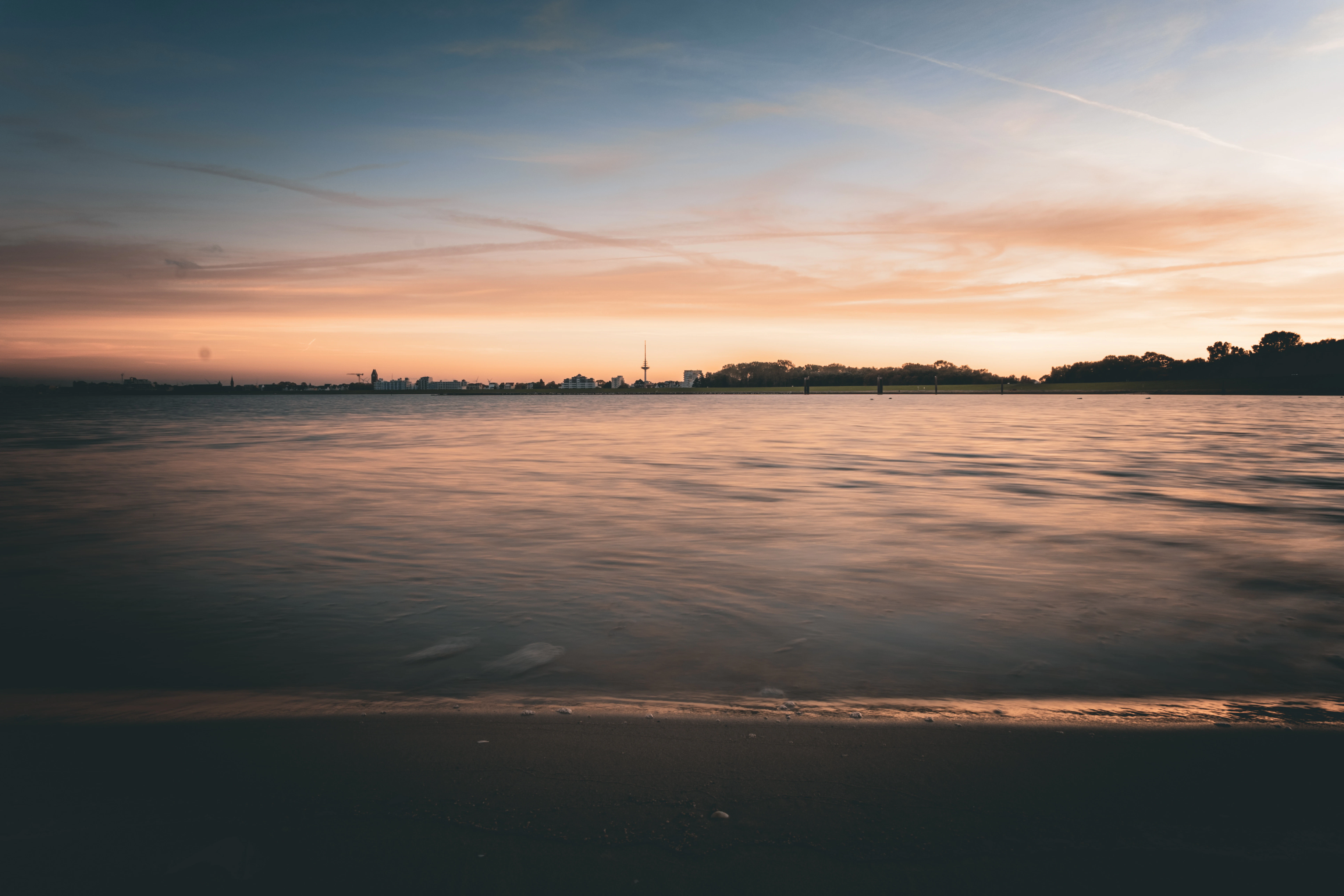 Calm ocean water at sunset with distant city skyline.