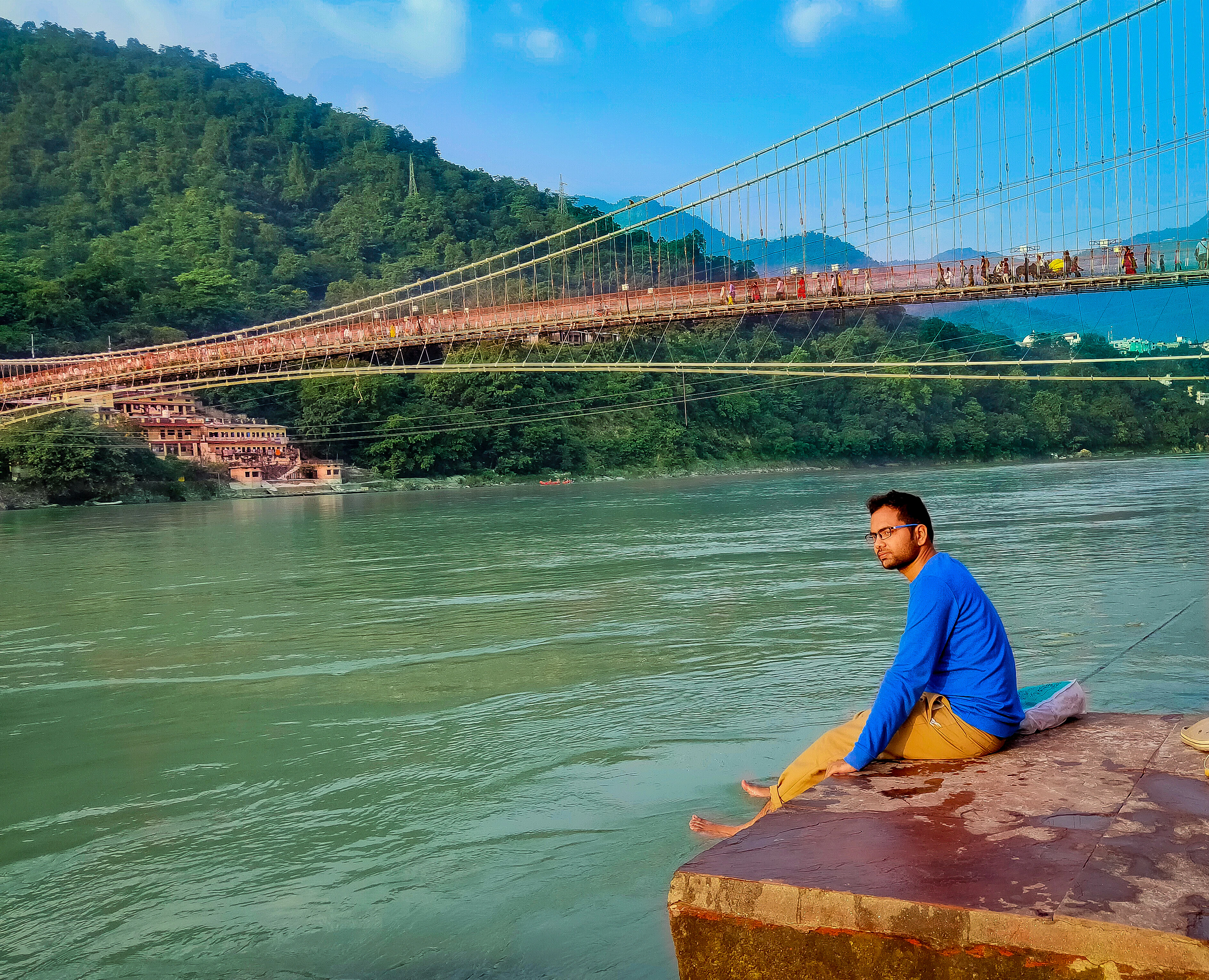 man in blue shirt sitting on brown rock near body of water during daytime