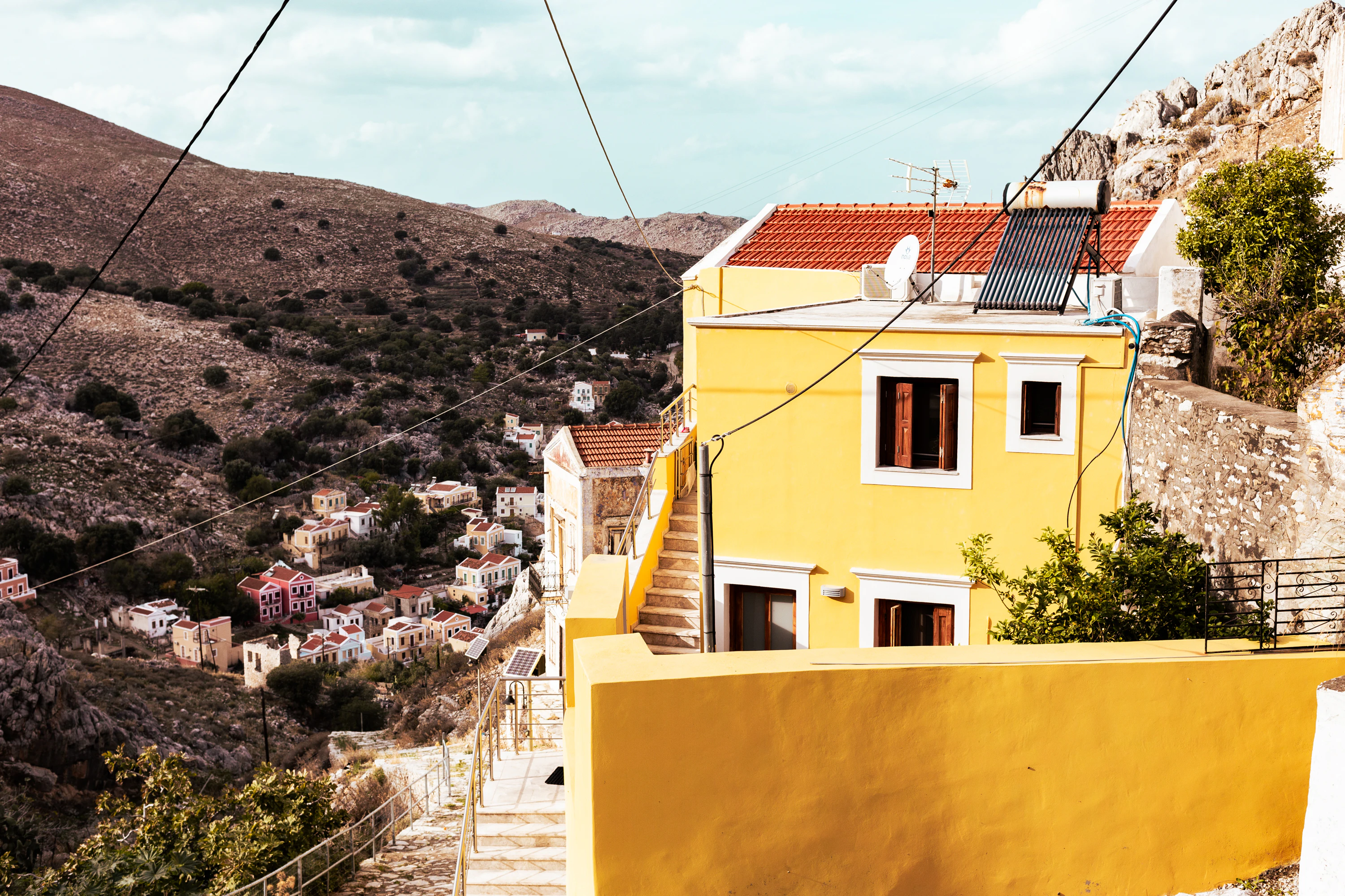 a yellow building with a red roof next to a hillside