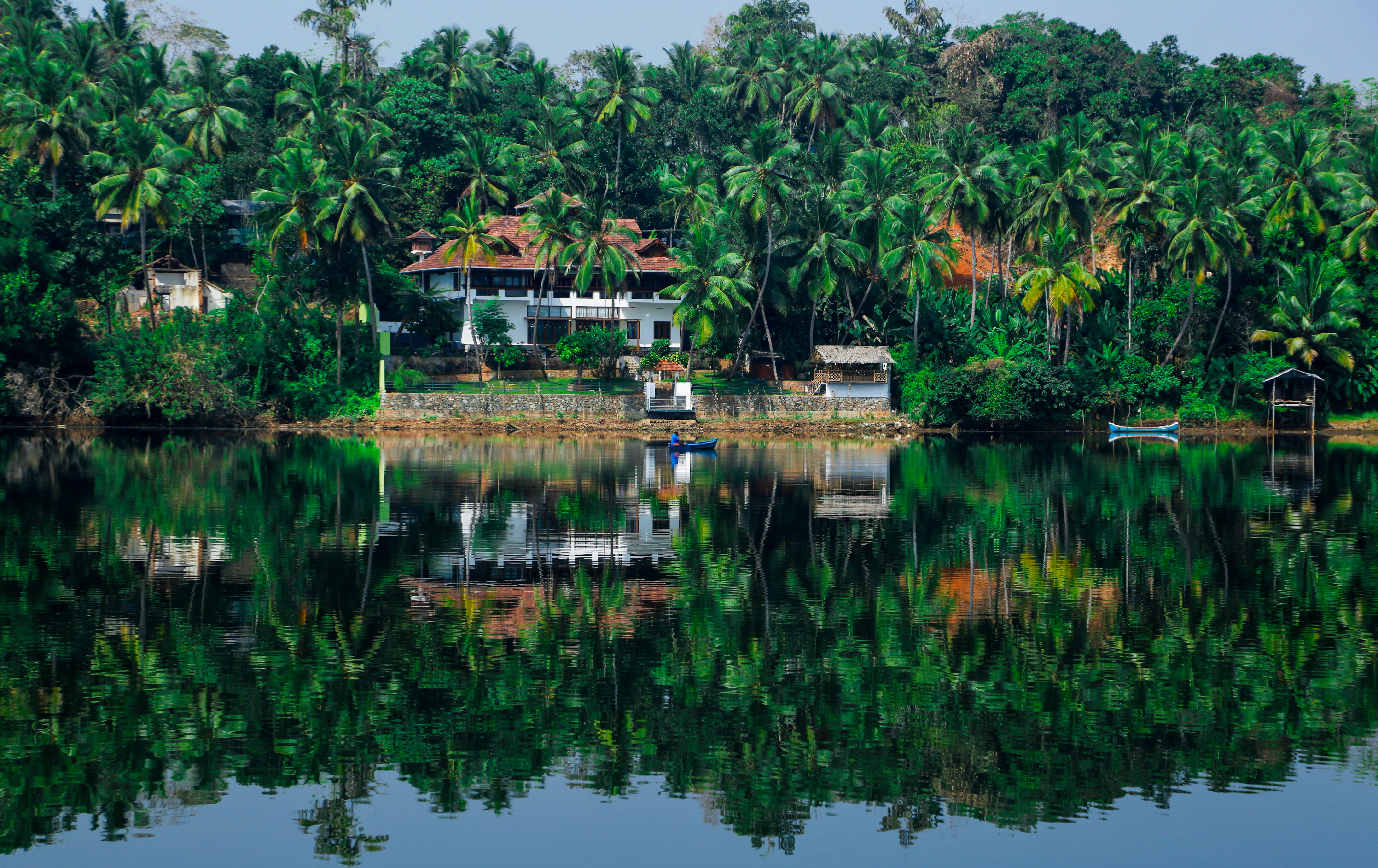 a house on the shore of a lake surrounded by palm trees