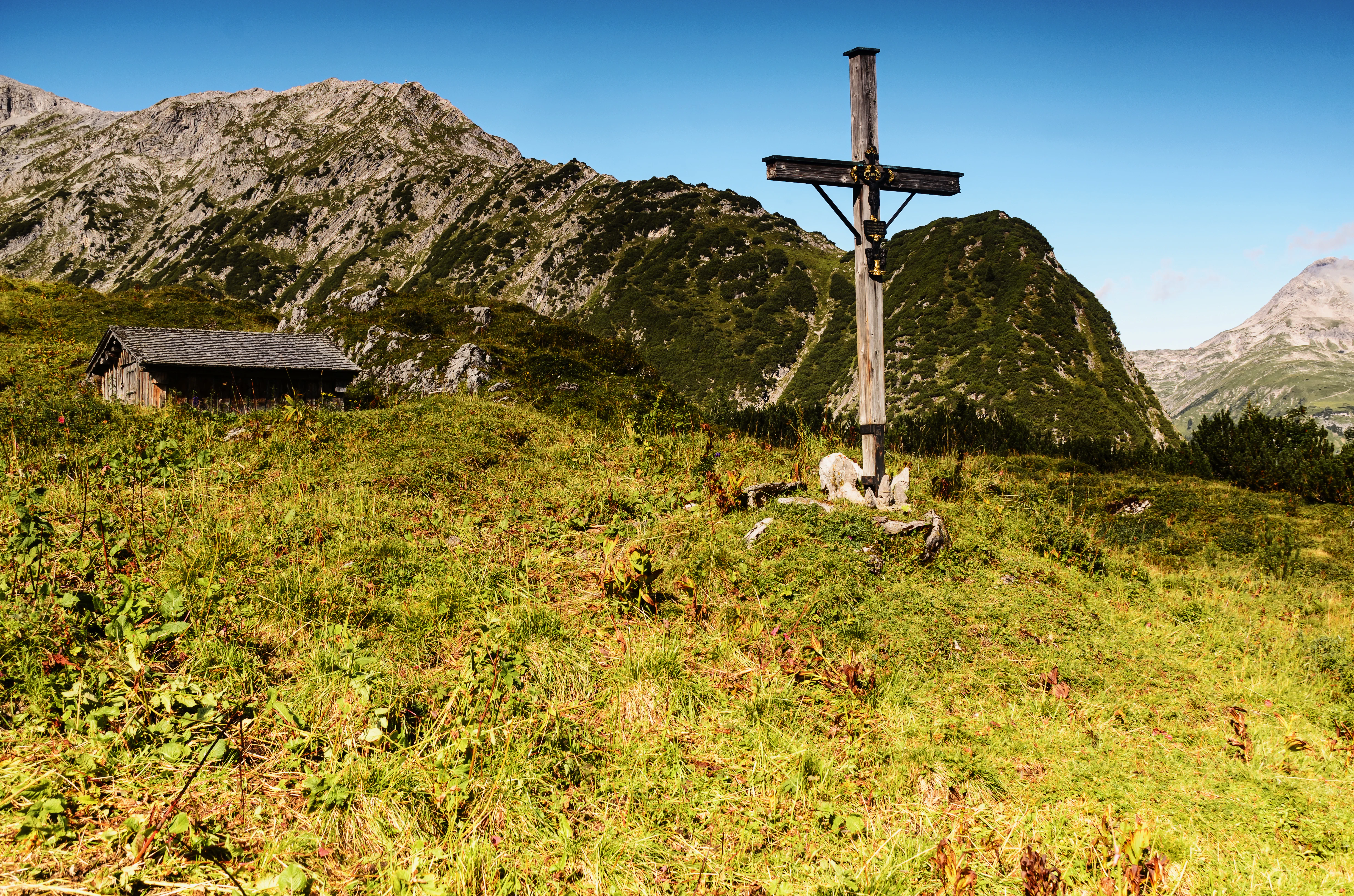 brown wooden cross on green grass field near gray rocky mountain under blue sky during daytime