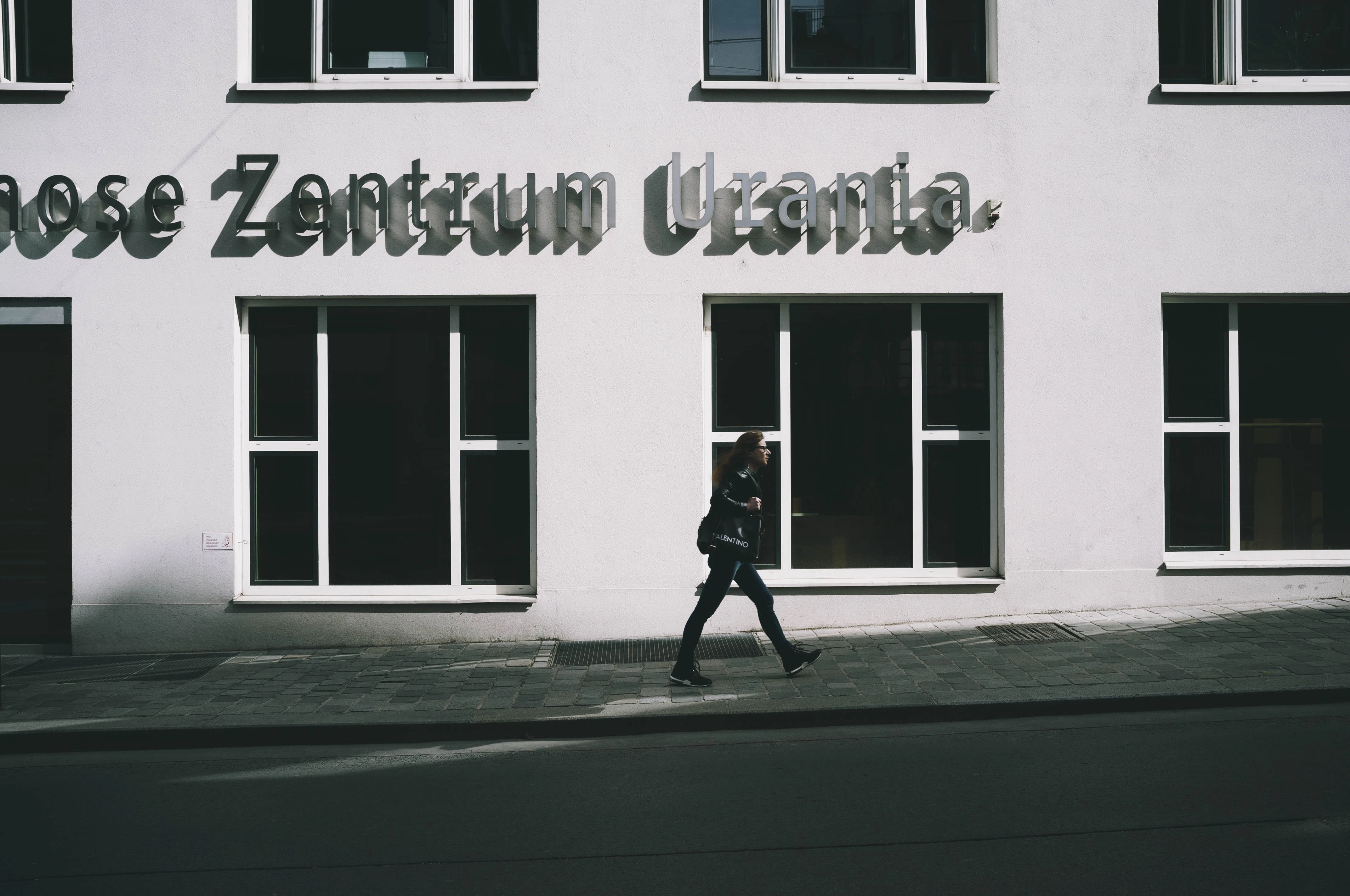 man in black jacket and pants walking on sidewalk in front of white and black building