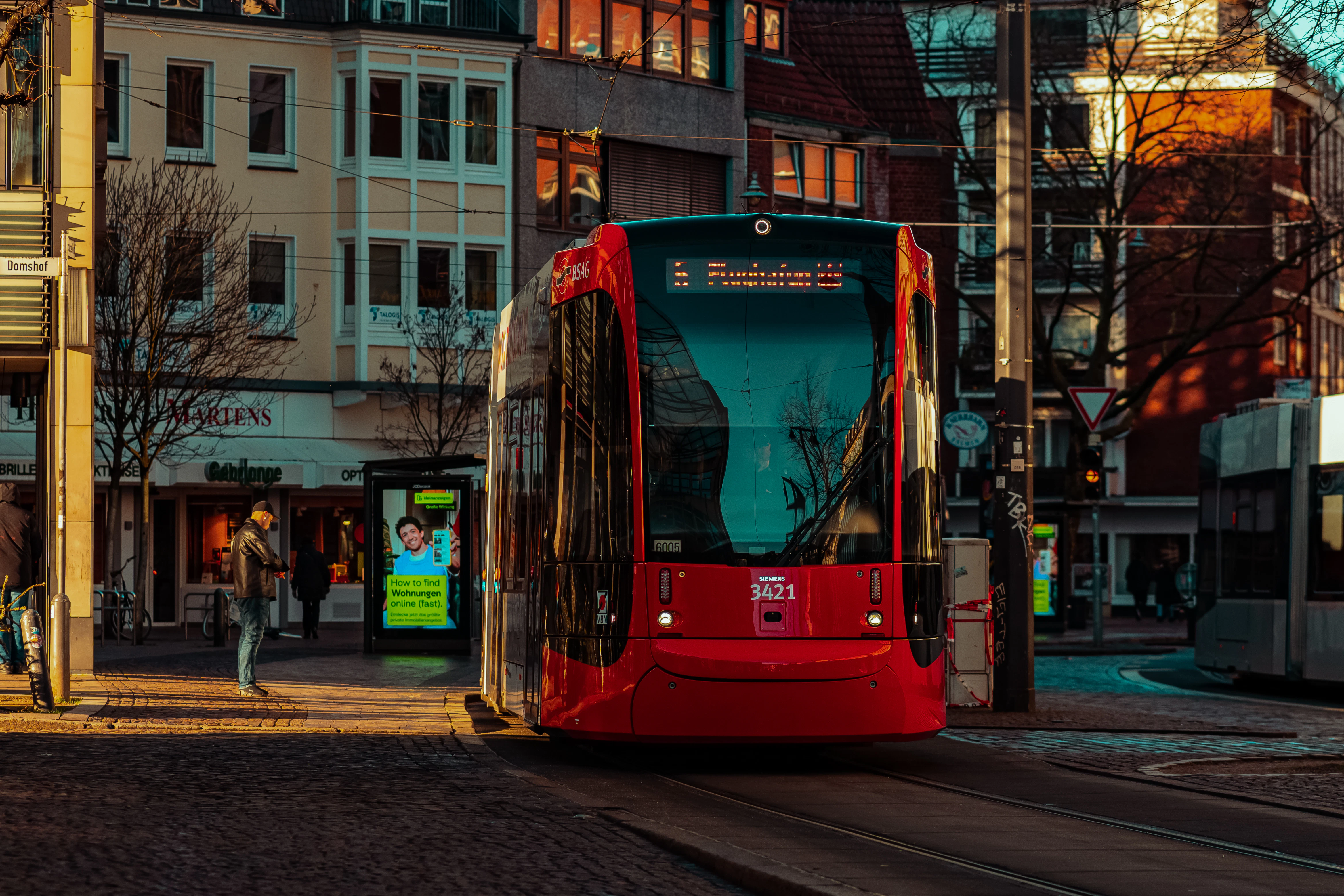A red bus driving down a street next to tall buildings